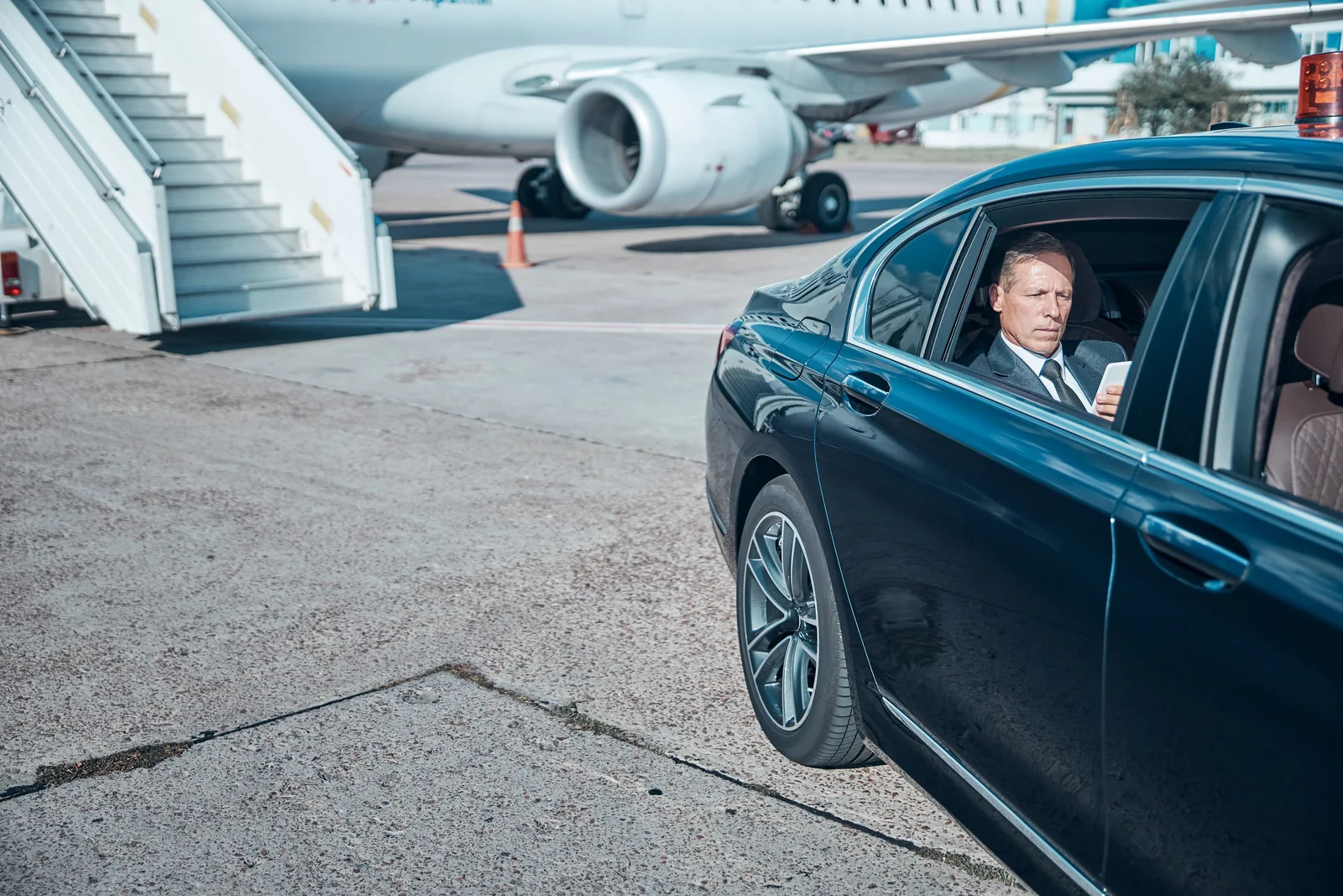 Business traveler reading a tablet in a car beside an aircraft